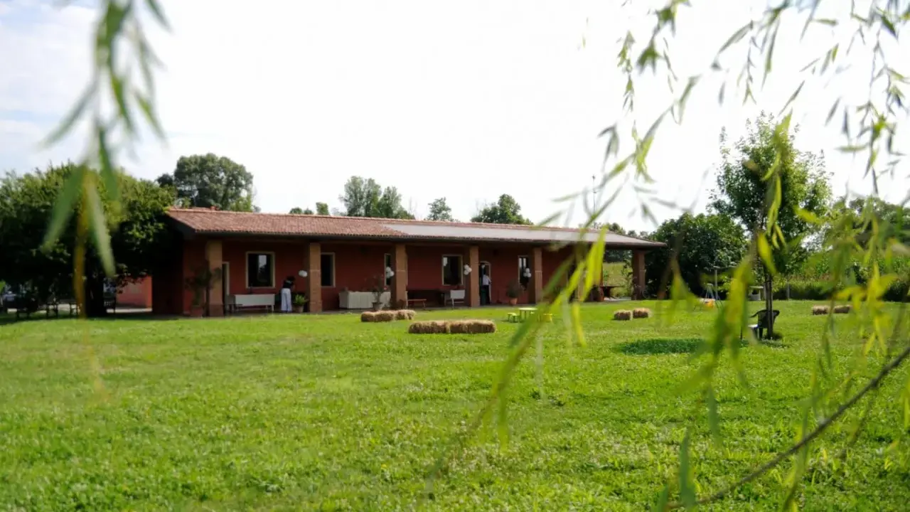 Un'accogliente fattoria didattica alle Fornaci, con un edificio rosso, balle di fieno e un prato verde.