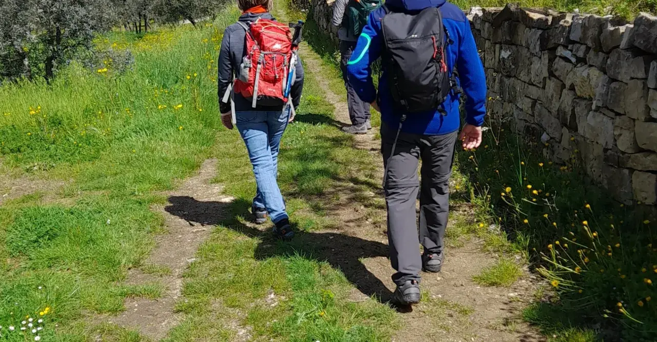 Persone con zaini fanno trekking in Toscana, vicino a Firenze, su un sentiero fiorito.
