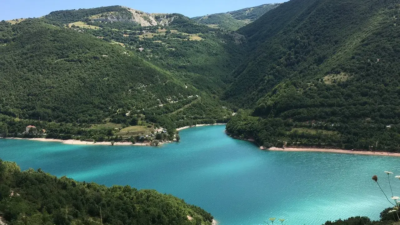 Un lago turchese incastonato tra colline verdi, ideale per il trekking nelle Marche.