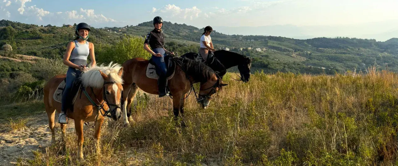 Tre ragazze in sella a cavalli godono di splendide passeggiate a cavallo in Abruzzo, tra colline verdi e cielo azzurro.