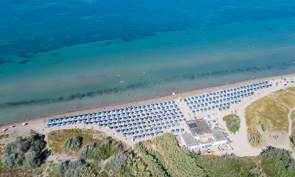 Spiaggia attrezzata con ombrelloni blu, ideale per campeggi in Toscana sul mare per bambini. Acqua cristallina e gente che si gode il sole.