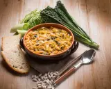 Piatto tipico toscano con pane raffermo: ribollita fumante in ciotola, contornata da fagioli, cavolo nero e porri.