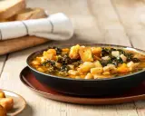 Una ciotola fumante di zuppa di cavolo nero e fagioli cannellini, guarnita con crostini dorati, su un tavolo di legno rustico.