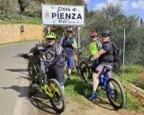 Quattro ciclisti si fermano per una foto con il cartello "Città di Pienza" durante un'avventura in bici nel Val d'Orcia.