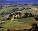 Colline ondulate e campi coltivati, un casale in mattoni rossi e cipressi svettanti, tipici delle **strade panoramiche toscana**.