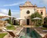 Piscina e lettini in una masseria per bambini in Puglia, con un antico edificio sullo sfondo.