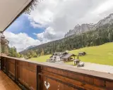 Vista da un balcone su una casa di montagna con prati verdi e boschi. Perfetta per una vacanza in montagna estate.