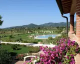 Un angolo di campagna toscana lungo il mare, con piscina, giardini curati e colline verdi all'orizzonte.