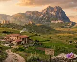 Agriturismi in Abruzzo montagna: un borgo con castelli domina la valle verdeggiante, con un casale fumante e un gregge al pascolo sotto il Gran Sasso.