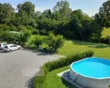Un **agricampeggio con piscina** immerso nel verde. Auto parcheggiate, camper, biciclette e persone che si rilassano all'ombra degli alberi. La piscina azzurra invita a un tuffo rinfrescante.