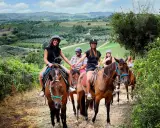 Un gruppo di amici si gode una **passeggiata a cavallo toscana** tra colline verdi e vigneti. Sorridono felici, immersi nella bellezza del paesaggio.