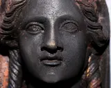 Volto di bronzo scuro, un dettaglio dei bronzi di San Casciano dei Bagni, con capelli a onde e trecce.