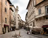 Un vicolo pittoresco tra i borghi vicino Montepulciano, con edifici storici, un leone scolpito su una colonna e tavolini all'aperto.