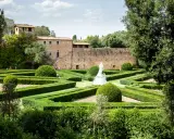 Giardino all'italiana con siepi geometriche, una statua bianca e un antico borgo toscano da visitare sullo sfondo.