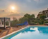 Piscina con lettini e gazebo, ideale per sapere dove dormire in Toscana. Tramonto suggestivo su un casale.