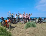 Un gruppo di ciclisti festeggia sulla spiaggia, pronti per un'avventura di cicloturismo in Toscana.