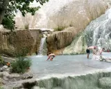 Persone si rilassano nelle piscine termali naturali di Castiglione d'Orcia, con cascate che scendono da rocce bianche.