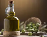 Bottiglia di olio extravergine di oliva, con olive verdi in cestino e su tagliere. La differenza tra olio di oliva e extravergine è la qualità.