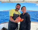 Coppia felice in barca, lui mostra un pesce rosso appena pescato, un'esperienza di pesca turismo indimenticabile.