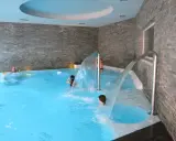 Bambini si divertono sotto cascate d'acqua in una piscina interna, un'ottima spa per famiglie in Lombardia.