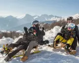 Famiglia felice in slittino sulla montagna per bambini in estate, con neve e montagne innevate sullo sfondo.