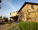 Un casale in pietra con rose rampicanti, un pergolato con tavoli e sedie, e cipressi svettano nel paesaggio della **Toscana in inverno**.
