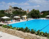 Piscina azzurra in un villaggio famiglie toscana, con castello medievale sullo sfondo e persone che si rilassano al sole.