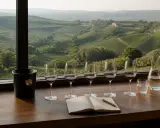 Calici di vino rosso pronti per una degustazione vini Langhe, con un taccuino aperto e un paesaggio collinare sullo sfondo.