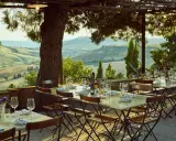 Tavoli apparecchiati sotto un pergolato con vista sulle colline toscane. Un'atmosfera perfetta per gustare i sapori degli agriturismi in Toscana.
