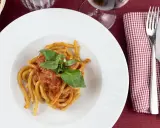 Pici al sugo, un classico della ricetta aglione Val di Chiana, serviti su un piatto bianco con basilico fresco.