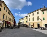 Piazza soleggiata a Pomarance, con edifici storici, tavolini all'aperto e scorci suggestivi da scoprire.