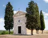 La chiesa di Vitaleta, con i suoi cipressi iconici, si erge solitaria su una collina toscana sotto un cielo azzurro.
