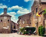 Un vicolo pittoresco a Sovana, Italia, con edifici in pietra, bandiere colorate e un cielo azzurro pieno di nuvole.