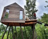 Un'esperienza unica per dormire nella natura toscana: una casa sull'albero in legno, con una persona che ammira il paesaggio dalla terrazza.