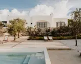 Piscina e lettini in una delle masserie famose puglia, con ulivi e cactus sotto un cielo azzurro con nuvole bianche.