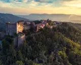 Antico castello medievale su una collina boscosa, uno dei tanti castelli da visitare in Toscana, con un villaggio arroccato e vista sulla valle al tramonto.
