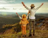 Bambini in Toscana, con le braccia al cielo, ammirano un paesaggio collinare al tramonto.