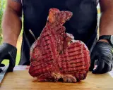 Un cuoco con guanti neri mostra una succulenta bistecca alla fiorentina appena grigliata, pronta per essere servita. Un esempio perfetto di come cucinare la bistecca alla fiorentina.