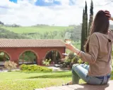 Donna con bicchiere di vino, vista su un casale con archi, paesaggio collinare. Un'oasi di pace tra gli agriturismi particolari Lombardia.