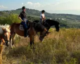 Tre ragazze in sella a cavalli godono di splendide passeggiate a cavallo in Abruzzo, tra colline verdi e cielo azzurro.
