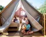 Bambini felici in un glamping: uno gioca col pallone, l'altro usa un tablet a letto. Avventura e relax per i più piccoli.