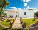 Un sentiero in pietra conduce a un bianco casolare, circondato da rocce granitiche e vegetazione mediterranea. Ideale per scoprire gli agriturismi Sardegna nord.