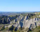 Paesaggio lunare con calanchi toscana, creste erose e vegetazione verdeggiante sotto un cielo azzurro.
