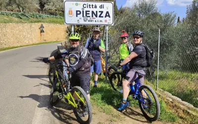 Quattro ciclisti si fermano per una foto con il cartello "Città di Pienza" durante un'avventura in bici nel Val d'Orcia.
