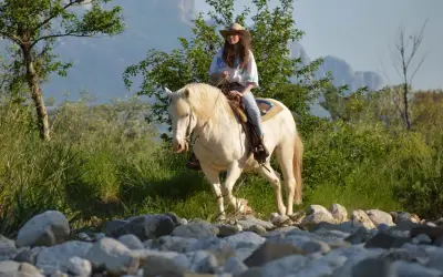 Giovane donna con cappello da cowboy e cavallo bianco durante una passeggiata a cavallo in Campania, tra rocce e vegetazione rigogliosa.