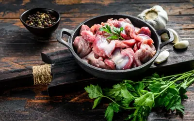 Piatto toscano con interiora di pollo crude in padella, con aglio, pepe e prezzemolo su tagliere di legno scuro.