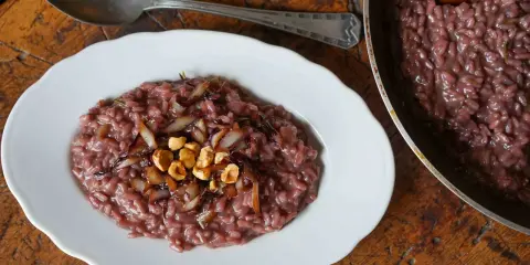 Risotto rosso con cipolla caramellata e nocciole, un classico tra i piatti tipici di Verona, servito su un piatto bianco con un cucchiaio d'argento.