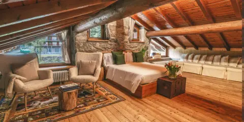 Accogliente camera con camino, travi in legno a vista, letto comodo, poltrone soffici e un tappeto decorato.