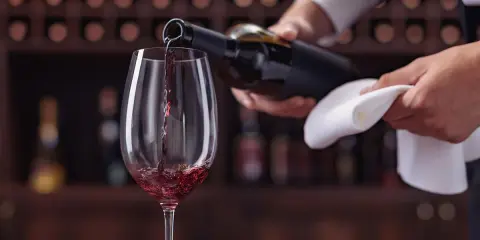 Un calice di vino rosso viene versato da una bottiglia, un momento perfetto per un tour enogastronomico Toscana.