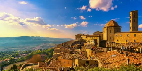 Un borgo toscano al tramonto, con tetti in cotto e un campanile svettante. Curiosità sulla Toscana: questo paesaggio evoca storie antiche.